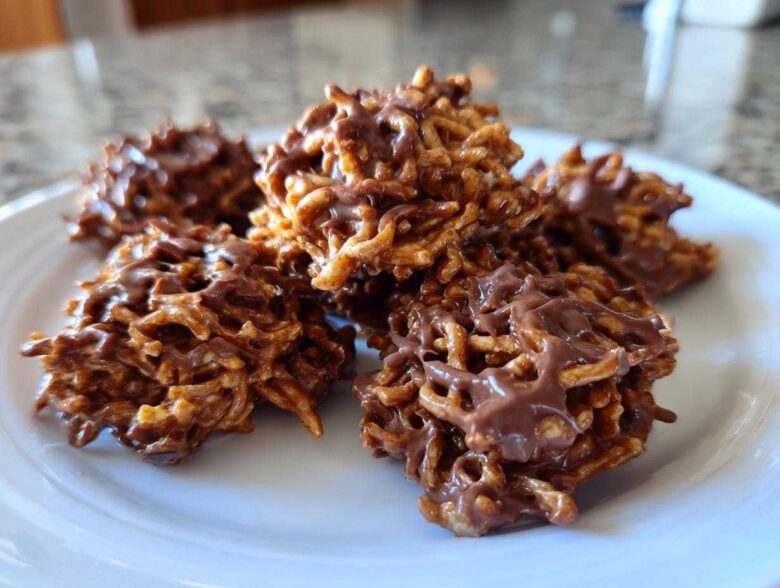 A close-up view of several freshly made chocolate haystack cookies piled on a white plate.