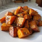 Close-up of beautifully caramelized roasted sweet potatoes seasoned with herbs on a white plate.