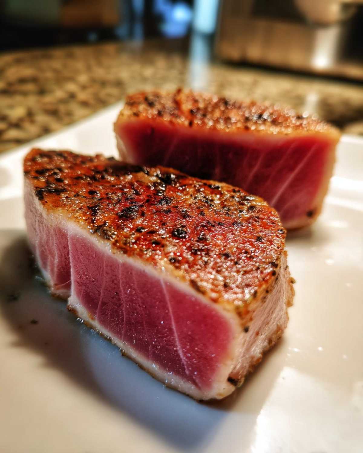 Two thick, perfectly seared Tuna Steaks showing a deep red, rare center and a dark, seasoned crust.