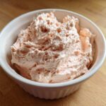Close-up of creamy, light pink tuna dip swirled high in a white ribbed bowl on a wooden surface.