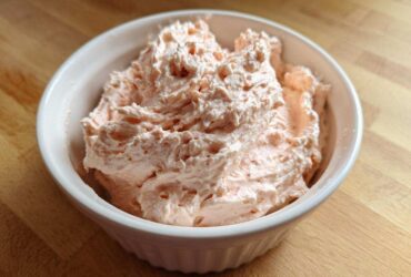 Close-up of creamy, light pink tuna dip swirled high in a white ribbed bowl on a wooden surface.