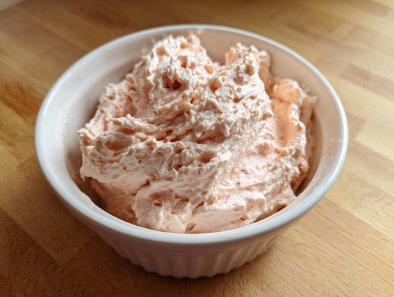 Close-up of creamy, light pink tuna dip swirled high in a white ribbed bowl on a wooden surface.