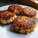Close-up of four perfectly pan-fried tuna fish cakes with a crispy, golden-brown crust served on a white plate.