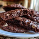 Close-up of gooey, fudgy andes mint cookies, one broken open showing melted chocolate chips and mint pieces.
