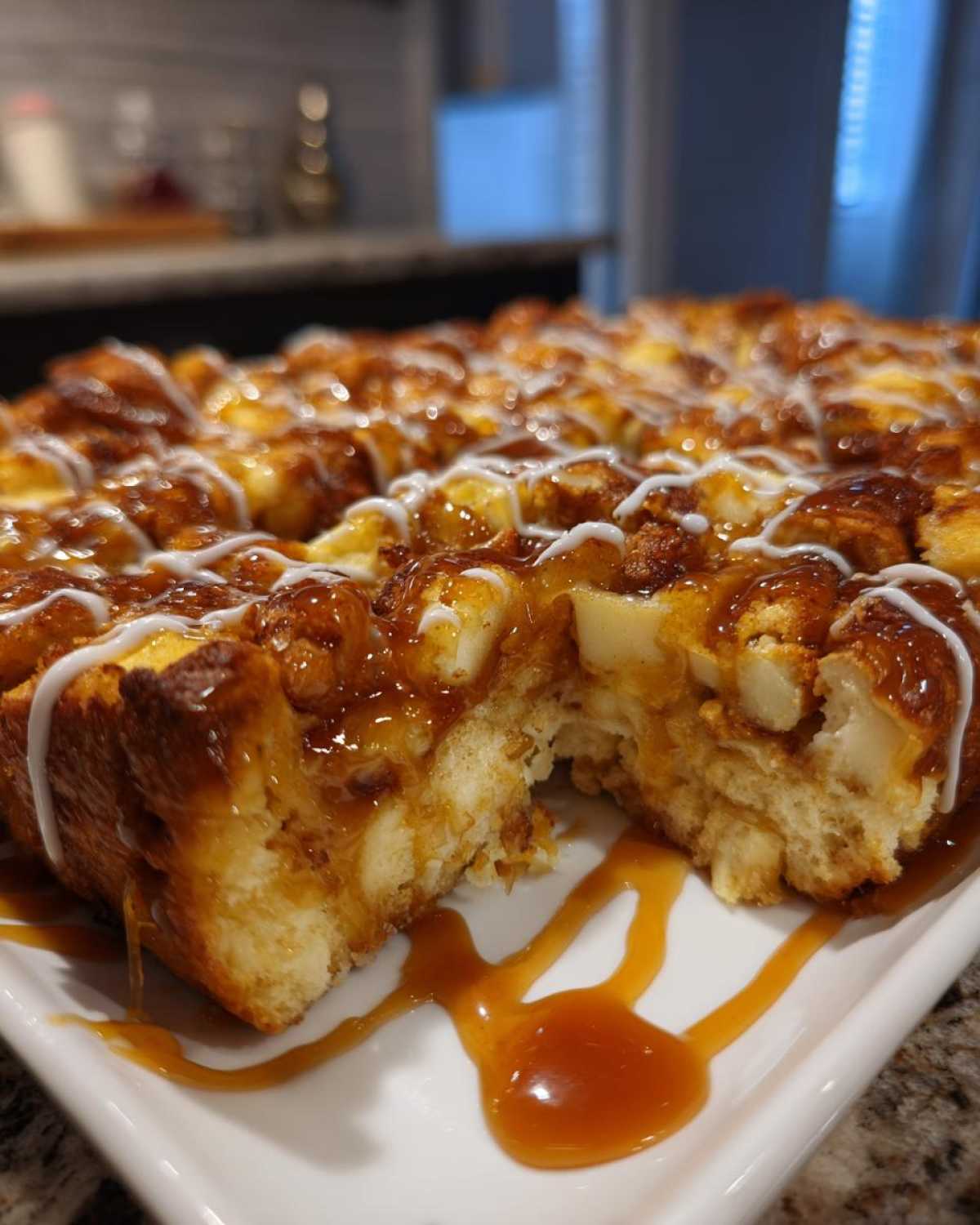 Close-up of a rich apple bread pudding topped with thick caramel sauce and white icing drizzle.