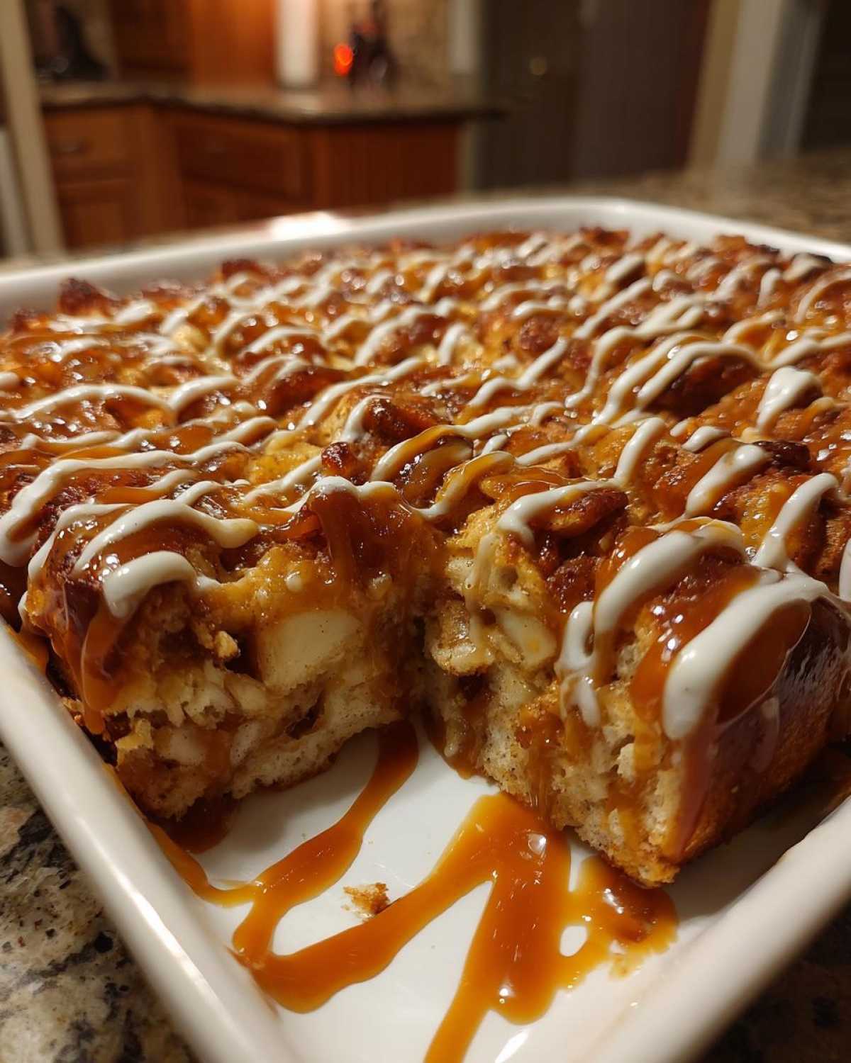 A square portion of rich apple bread pudding, drizzled heavily with caramel and white icing.
