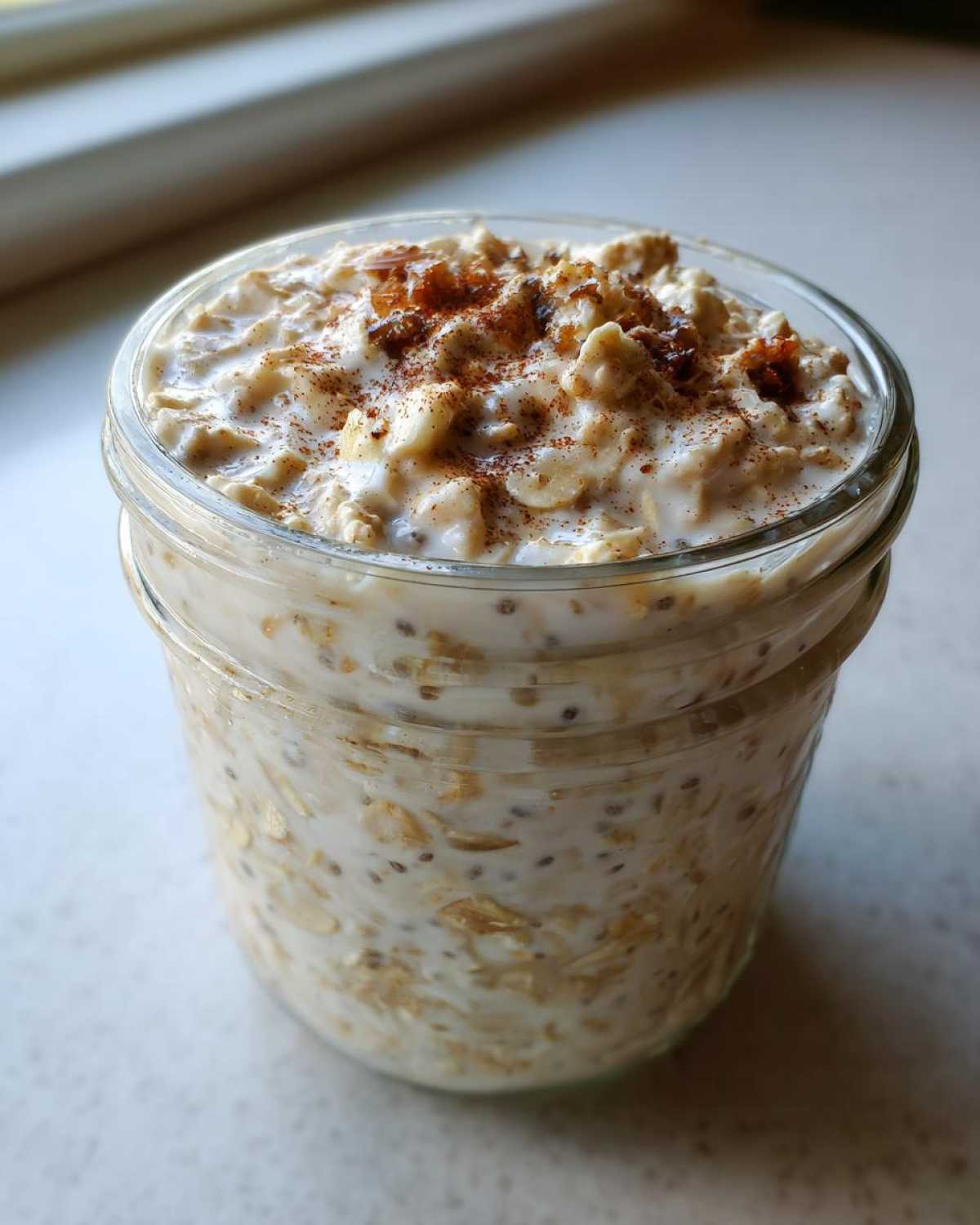 A glass jar filled with creamy apple cinnamon overnight oats, topped with cinnamon and a drizzle of syrup.