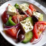 A vibrant close-up of an authentic greek salad featuring large chunks of feta cheese, tomatoes, cucumbers, red onion, and Kalamata olives.