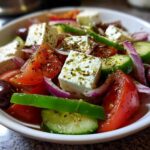 Close-up of a vibrant bowl of authentic greek salad featuring large cubes of feta, tomatoes, cucumbers, red onion, and Kalamata olives.