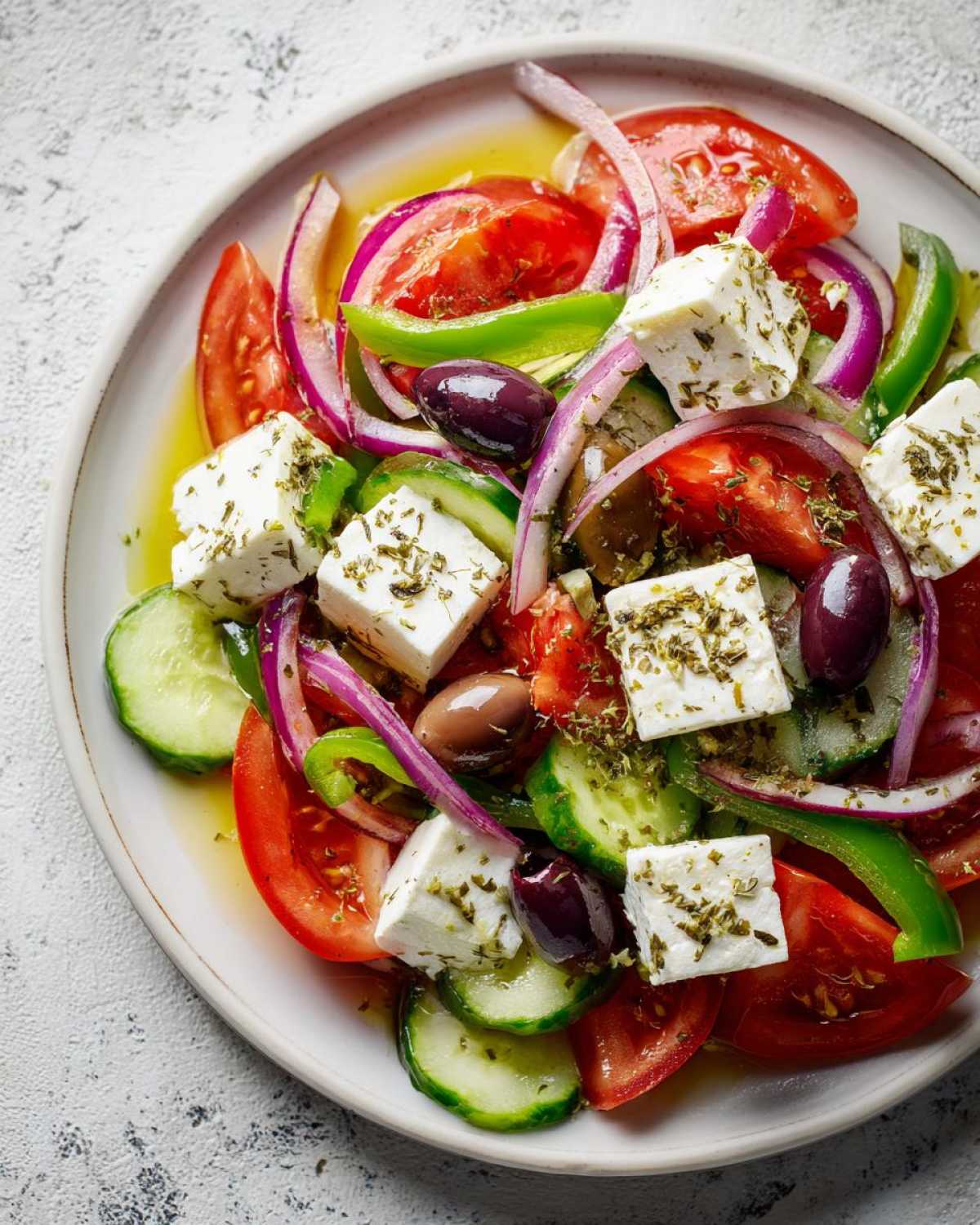 Overhead view of a vibrant greek salad featuring large cubes of feta, sliced tomatoes, cucumbers, red onion, and Kalamata olives.