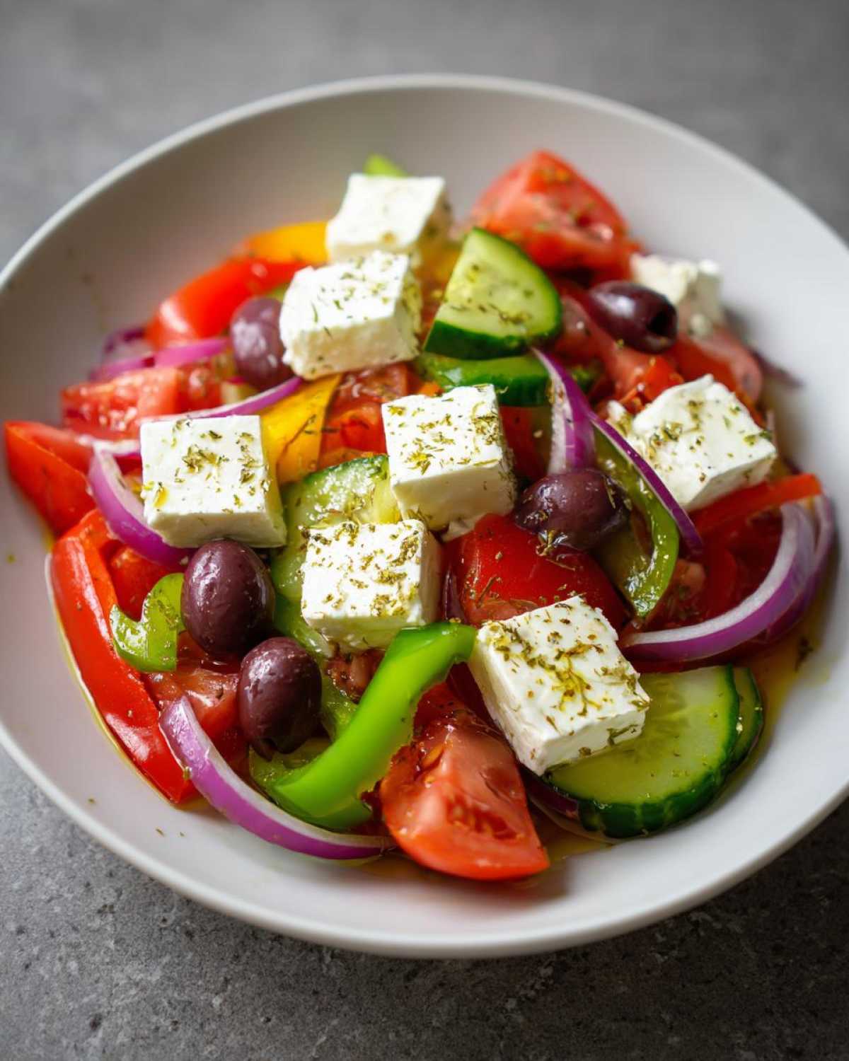 Close-up of a vibrant greek salad featuring large cubes of feta cheese, tomatoes, cucumbers, red onion, and Kalamata olives.