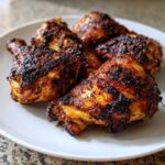 Close-up of several baked jamaican jerk chicken pieces with a dark, caramelized, and slightly charred crust.