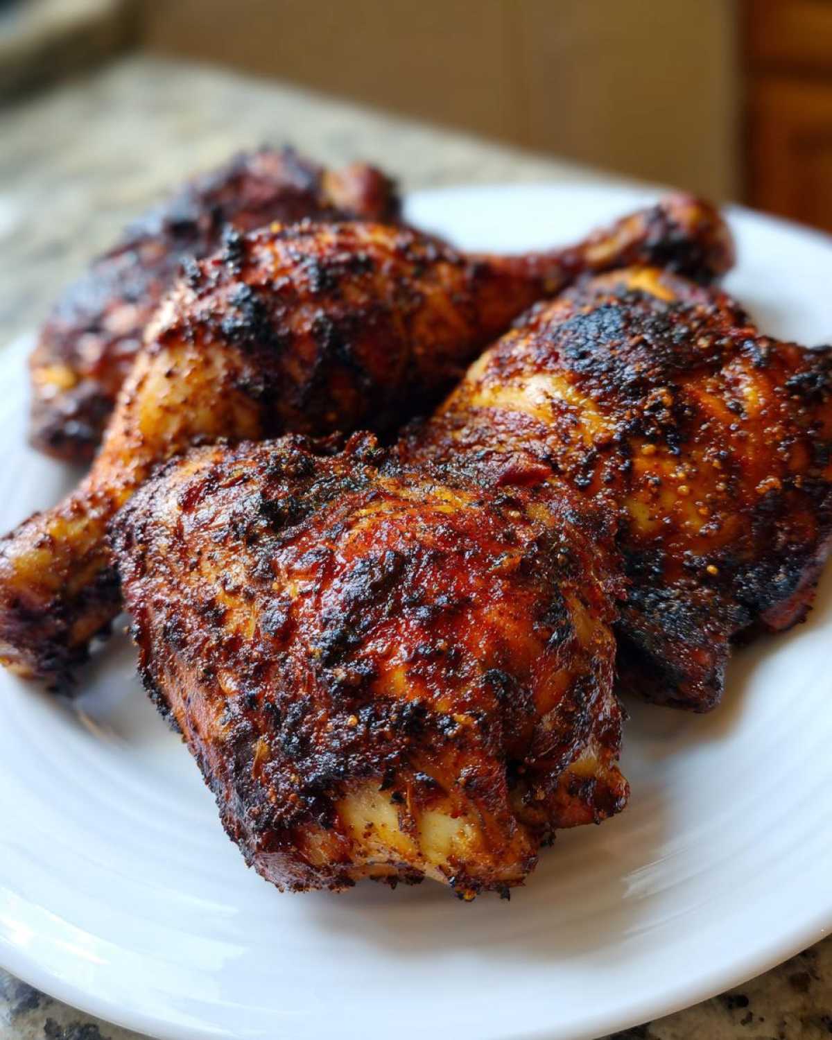 Four pieces of baked jamaican jerk chicken with a dark, spicy crust served on a white plate.