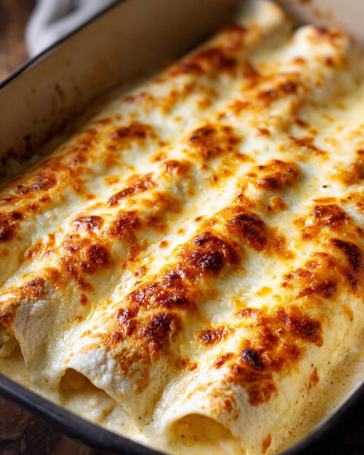 Close-up of baked white chicken enchiladas covered in bubbly, browned Monterey Jack cheese sauce.