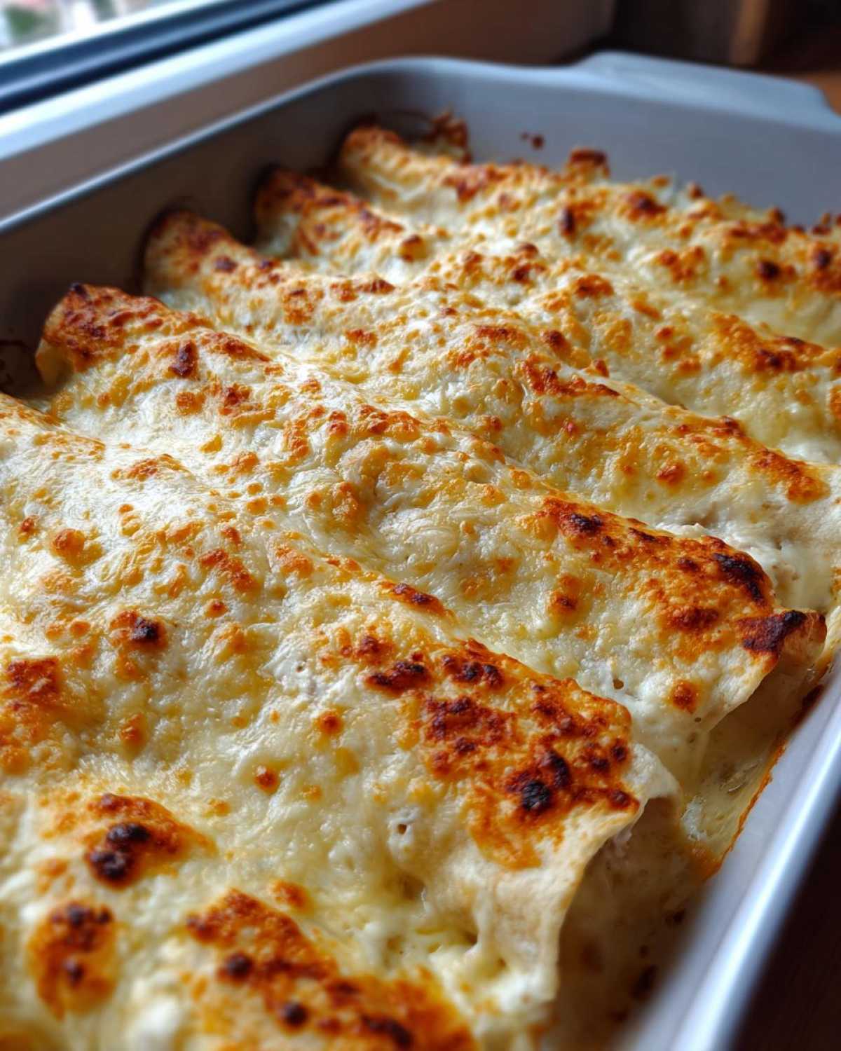 Close-up of freshly baked white chicken enchiladas covered in bubbly, browned cheese sauce.