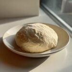 A smooth, round ball of pale fufu dough resting on a light-colored plate.