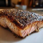 Close-up of a thick, perfectly cooked piece of blackened salmon showing a dark, seasoned crust and flaky pink interior.