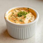 A small white ramekin filled with creamy, orange-hued remoulade sauce, topped with fresh parsley.