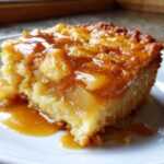 Close-up of a moist slice of caramel apple dump cake topped with gooey caramel sauce and cooked apples.