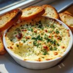 A hot, bubbly, cheesy bread dip topped with parsley, served with toasted bread slices.