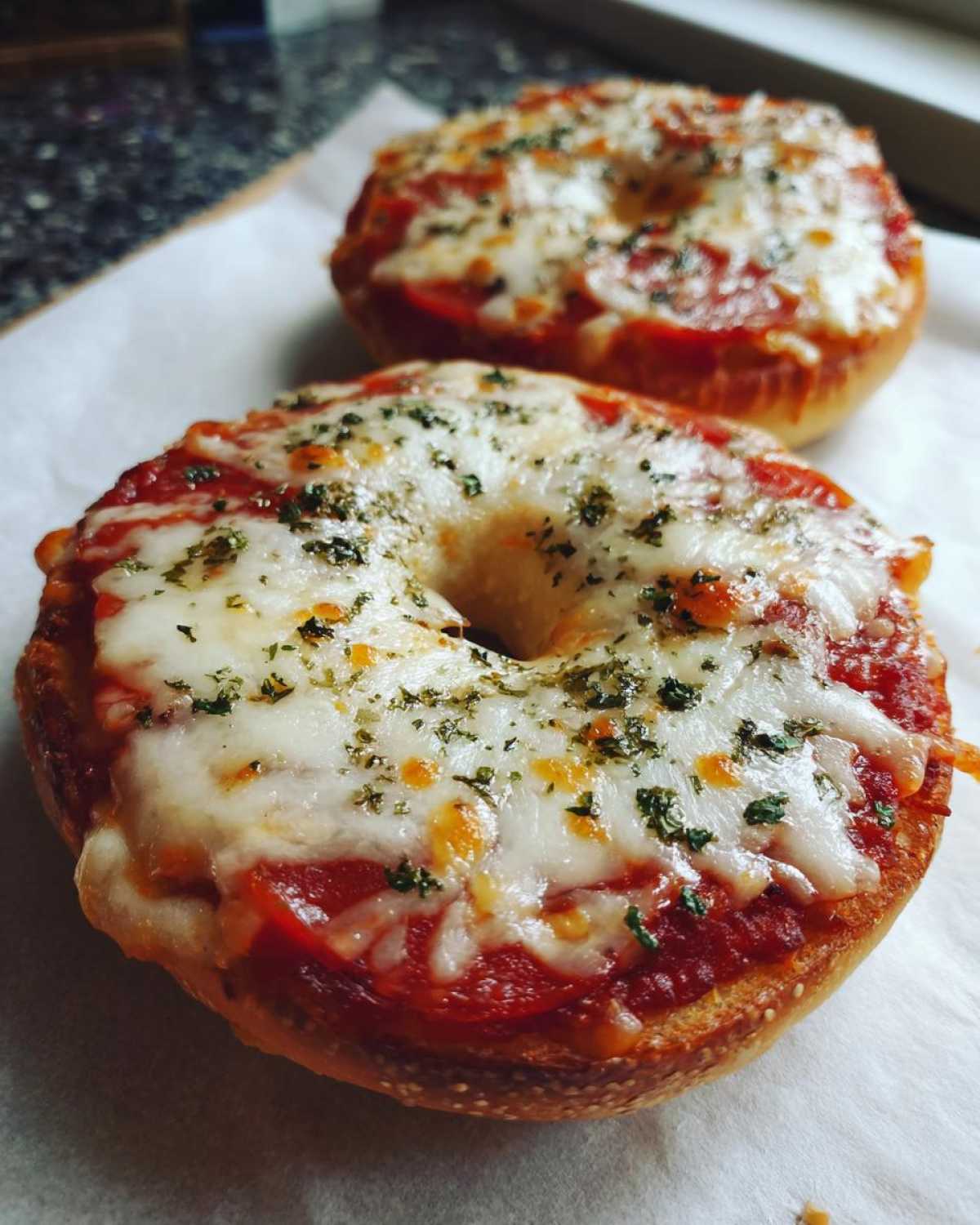 A close-up of two freshly baked pizza bagels topped with melted mozzarella, pepperoni, and herbs.