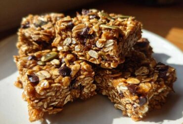Close-up of stacked, chewy homemade granola bars packed with oats, chocolate chips, and pumpkin seeds.