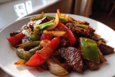 A close-up shot of glistening Chinese pepper steak featuring tender beef strips mixed with bright red and green bell peppers and onions.