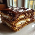 A close-up of a decadent slice of chocolate eclair cake showing graham cracker layers, white cream filling, and rich chocolate frosting.