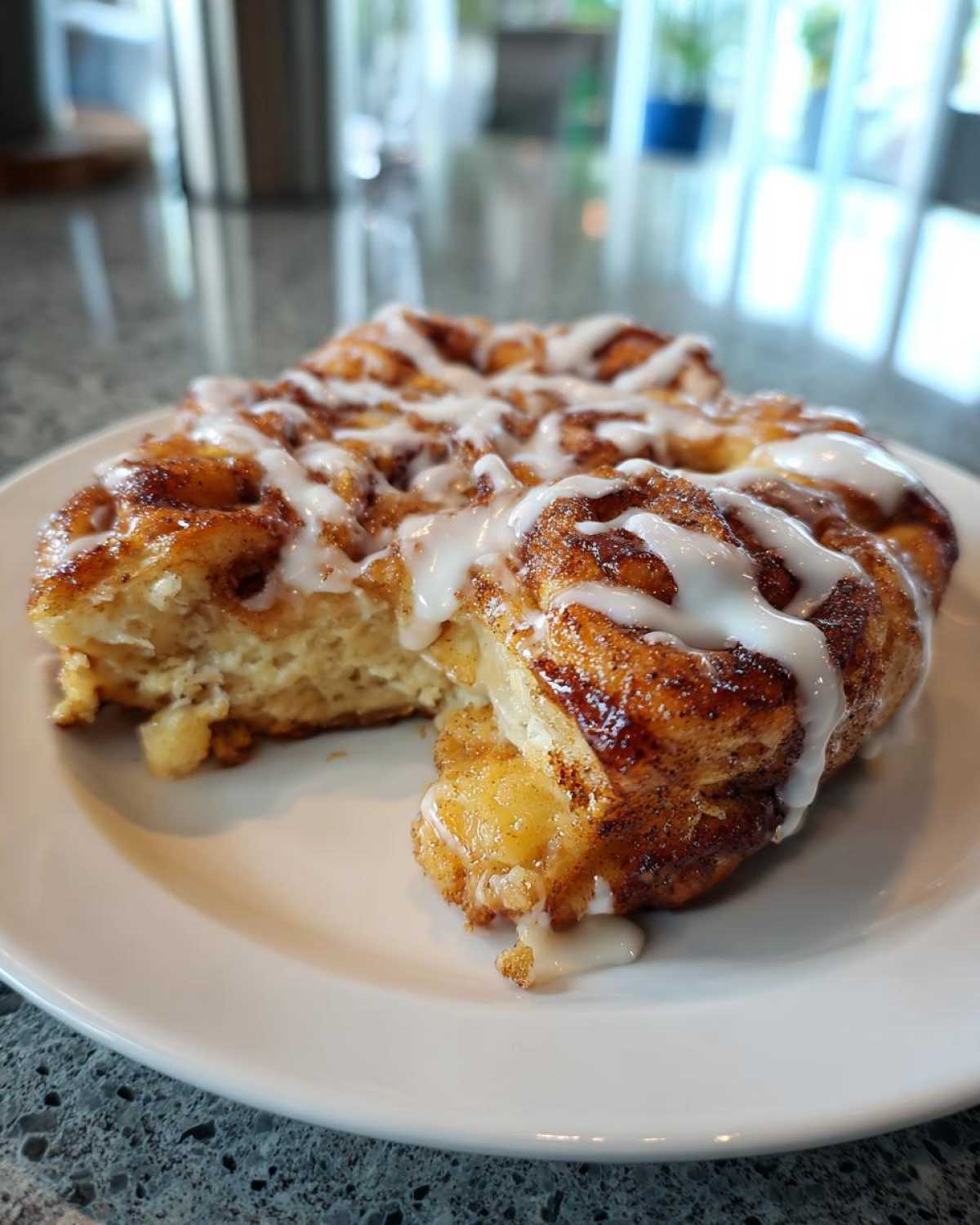 A close-up of a portion of cinnamon roll apple pie, drizzled heavily with white icing.