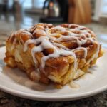 A close-up of a single serving of cinnamon roll apple pie, drizzled with white icing.