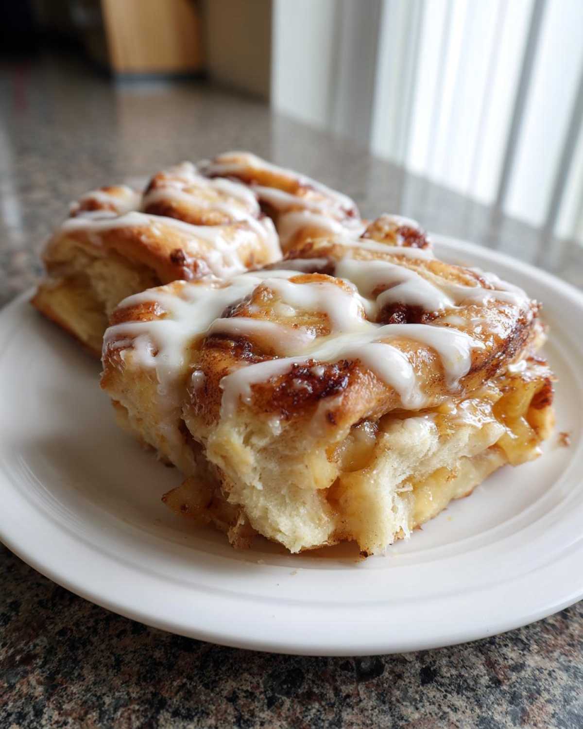 Two servings of gooey cinnamon roll apple pie squares topped with white icing on a white plate.