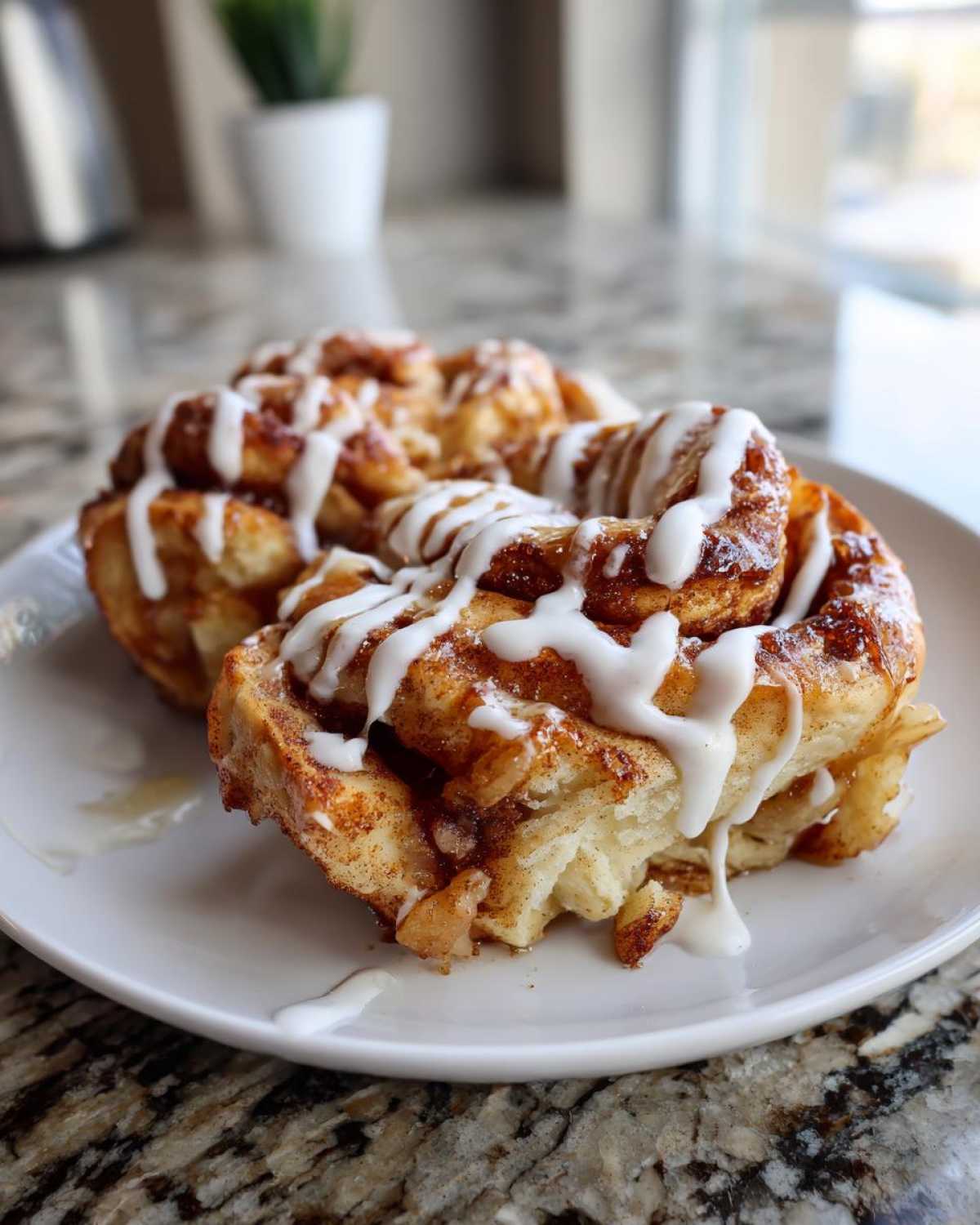 Two gooey swirls of cinnamon roll apple pie topped with thick white icing, sitting on a white plate.