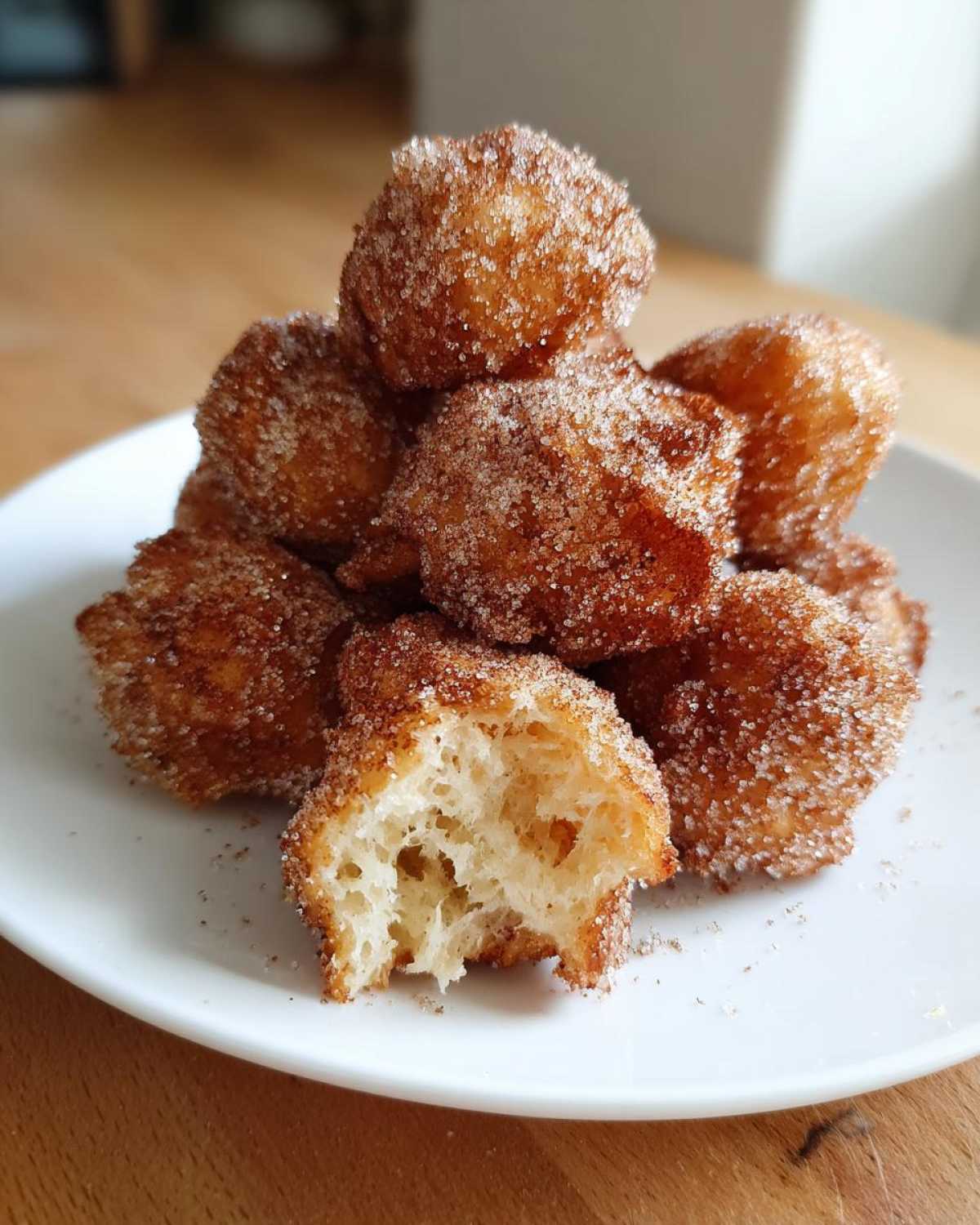 A pile of golden brown buñuelos coated in cinnamon sugar, with one broken open showing the fluffy interior.