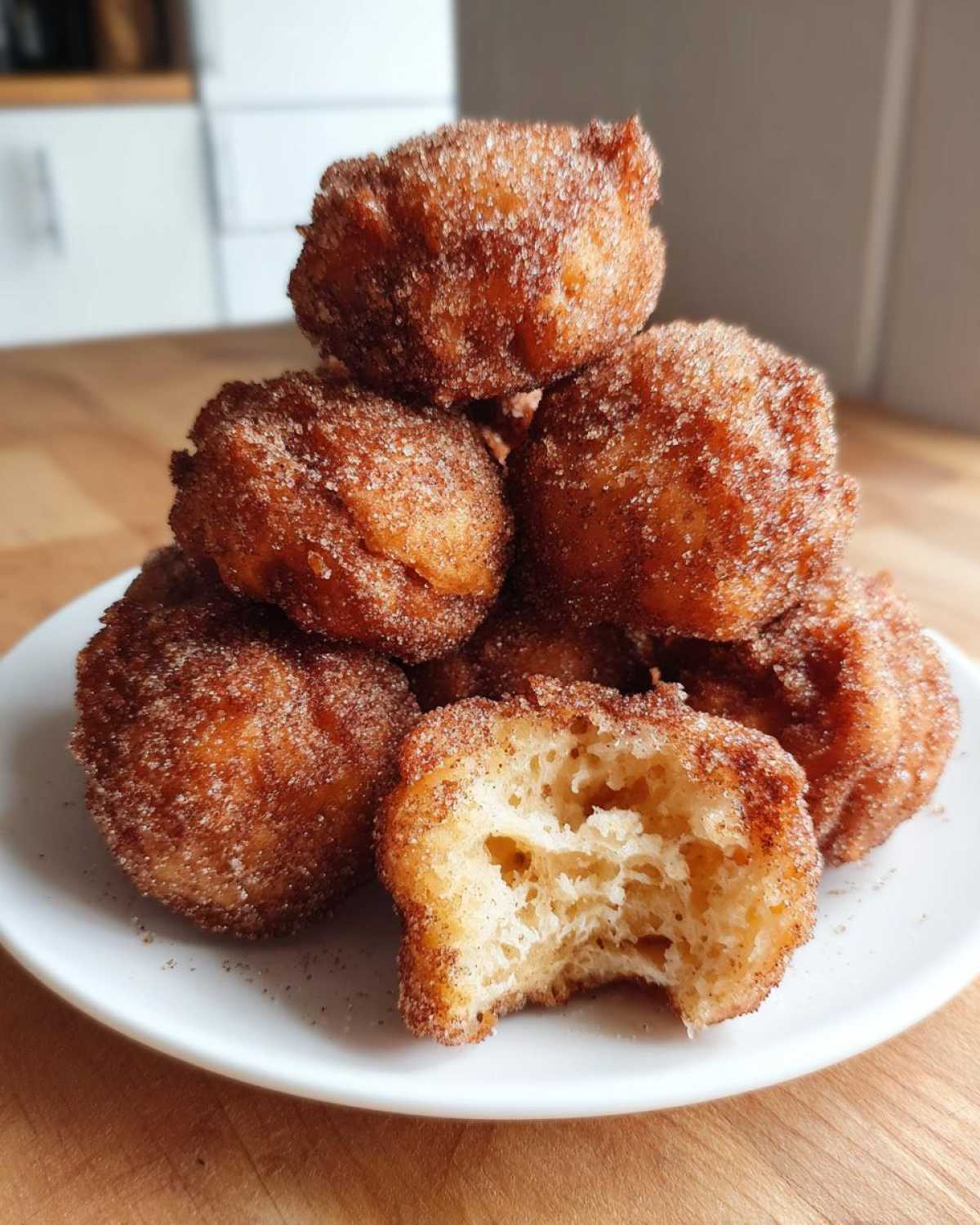 A stack of golden brown buñuelos coated in cinnamon sugar, with one piece broken open showing the fluffy interior.