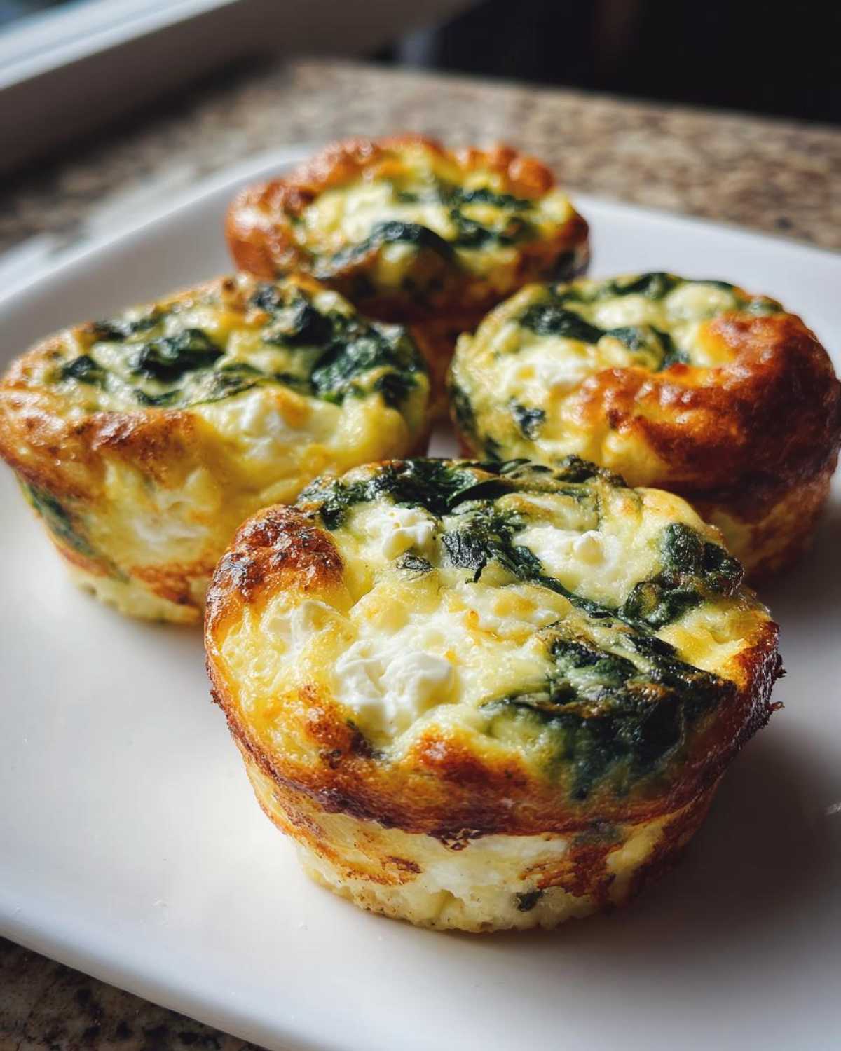 Four golden-brown Cottage Cheese Egg Cups With Spinach & Feta served on a white plate.