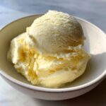Two scoops of creamy, pale yellow banana ice cream served in a small, light-colored bowl.