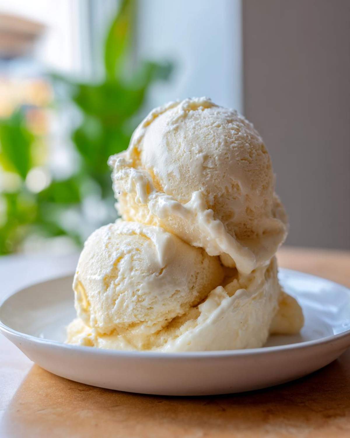 Two scoops of creamy, pale yellow banana ice cream stacked in a white bowl.