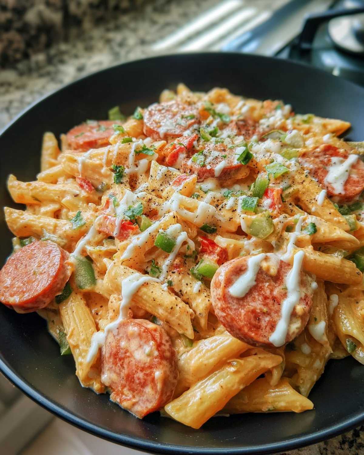 Close-up of creamy cajun sausage pasta with penne, sliced sausage, peppers, and a white sauce drizzle.