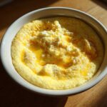 A close-up of creamy cheese grits topped with melted butter and extra cheese in a white bowl.