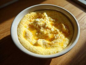 A close-up of creamy cheese grits topped with melted butter and extra cheese in a white bowl.