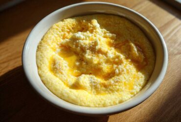 A close-up of creamy cheese grits topped with melted butter and extra cheese in a white bowl.