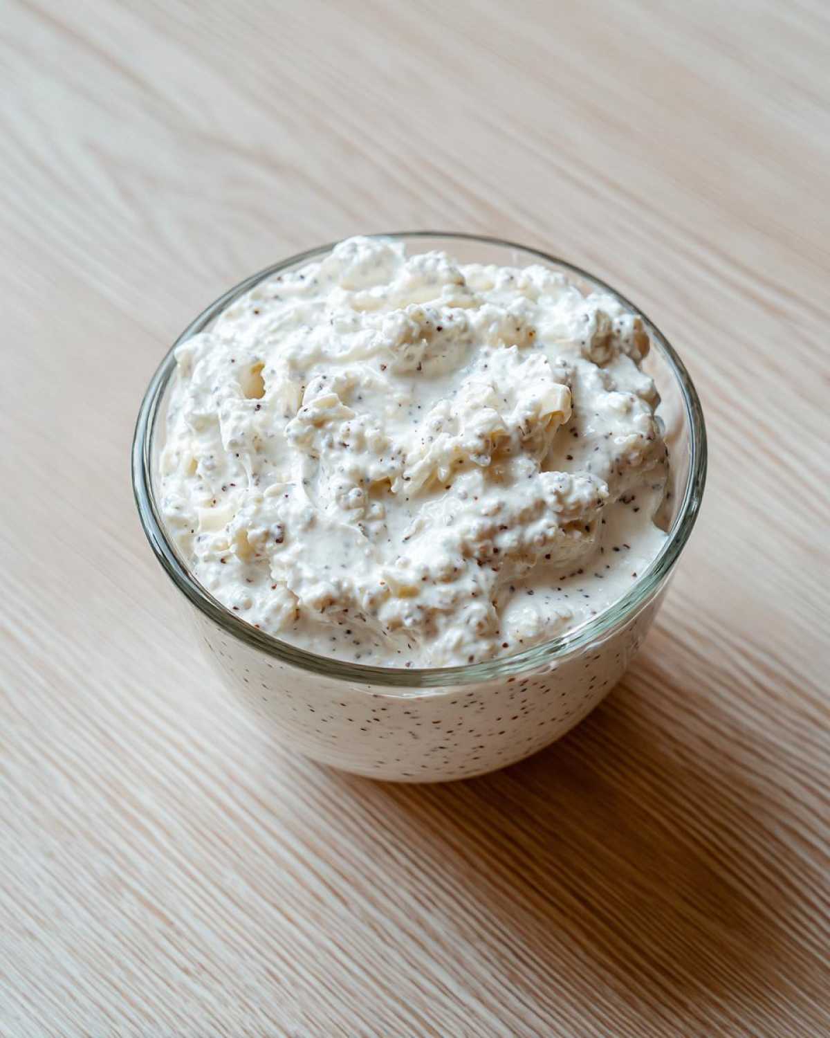 A close-up of thick, creamy coconut chia pudding speckled with dark chia seeds in a clear glass bowl.