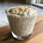 Close-up of creamy coconut chia pudding topped with crunchy golden bits in a clear glass.