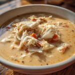 Close-up of a bowl of rich, creamy crab soup generously topped with large flakes of white and orange crab meat.