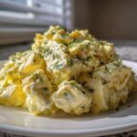 A mound of creamy egg salad, featuring large chunks of egg coated in yellow dressing and sprinkled with fresh dill.