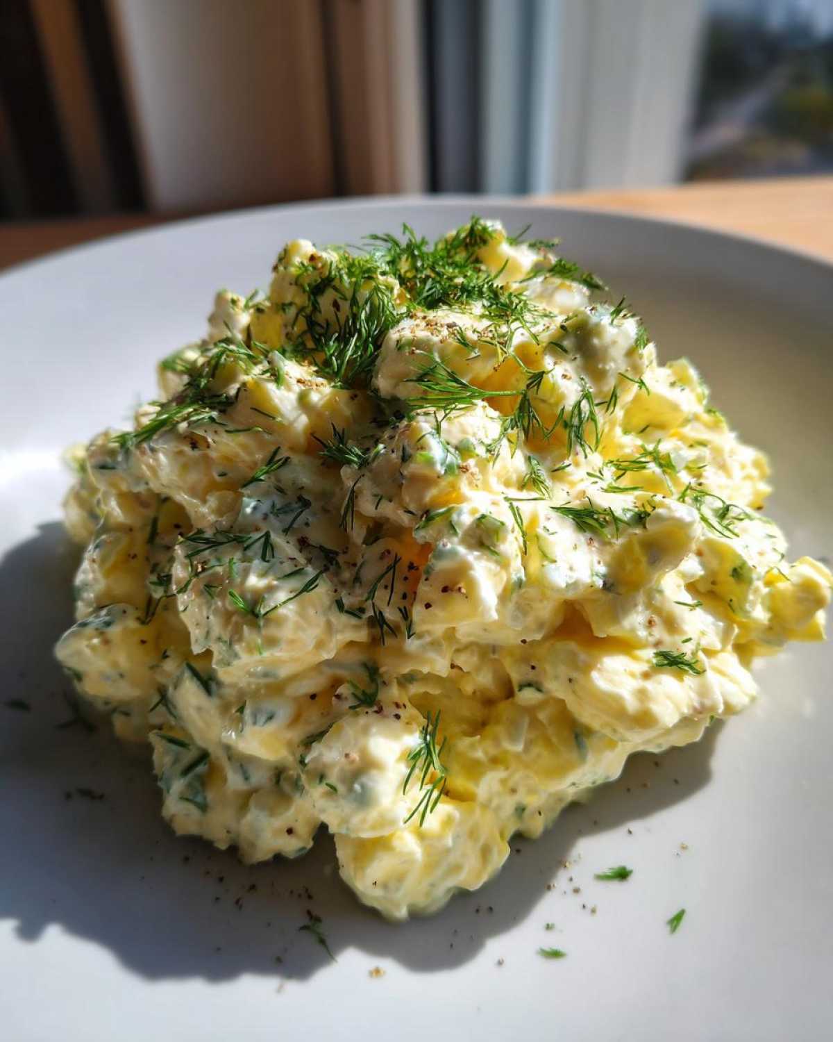 A mound of creamy egg salad generously topped with fresh dill and cracked black pepper on a white plate.