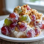 Close-up of a serving of creamy grape salad chick style, featuring red and green grapes coated in dressing and topped with crushed nuts.