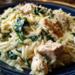 Close-up of creamy lemon chicken orzo mixed with wilted spinach and chunks of seasoned chicken breast.