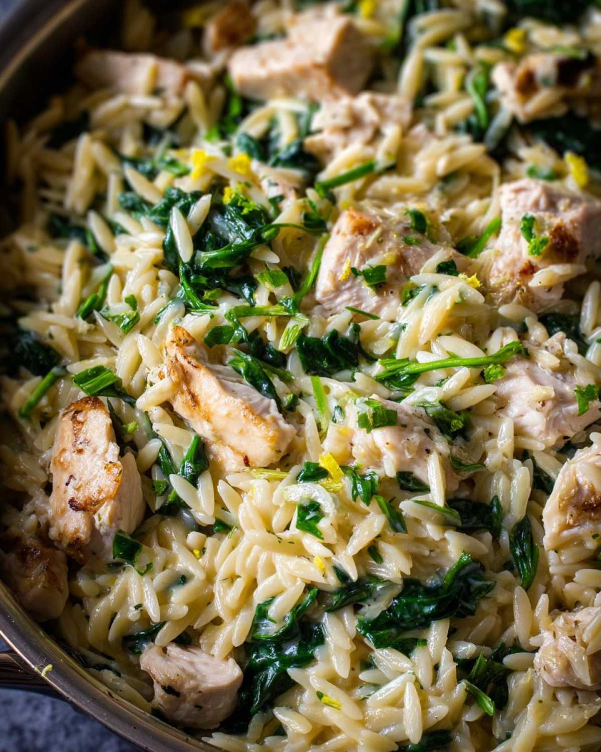 Close-up of creamy lemon chicken orzo mixed with wilted spinach and bright lemon zest.