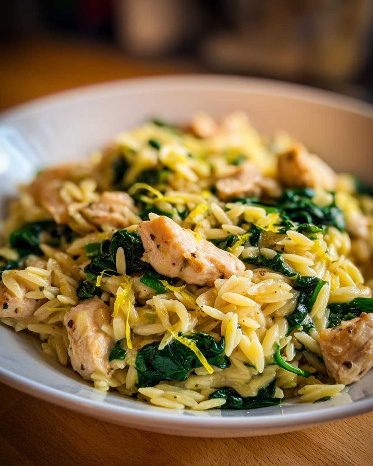A close-up of creamy lemon chicken orzo mixed with wilted spinach and topped with bright lemon zest.